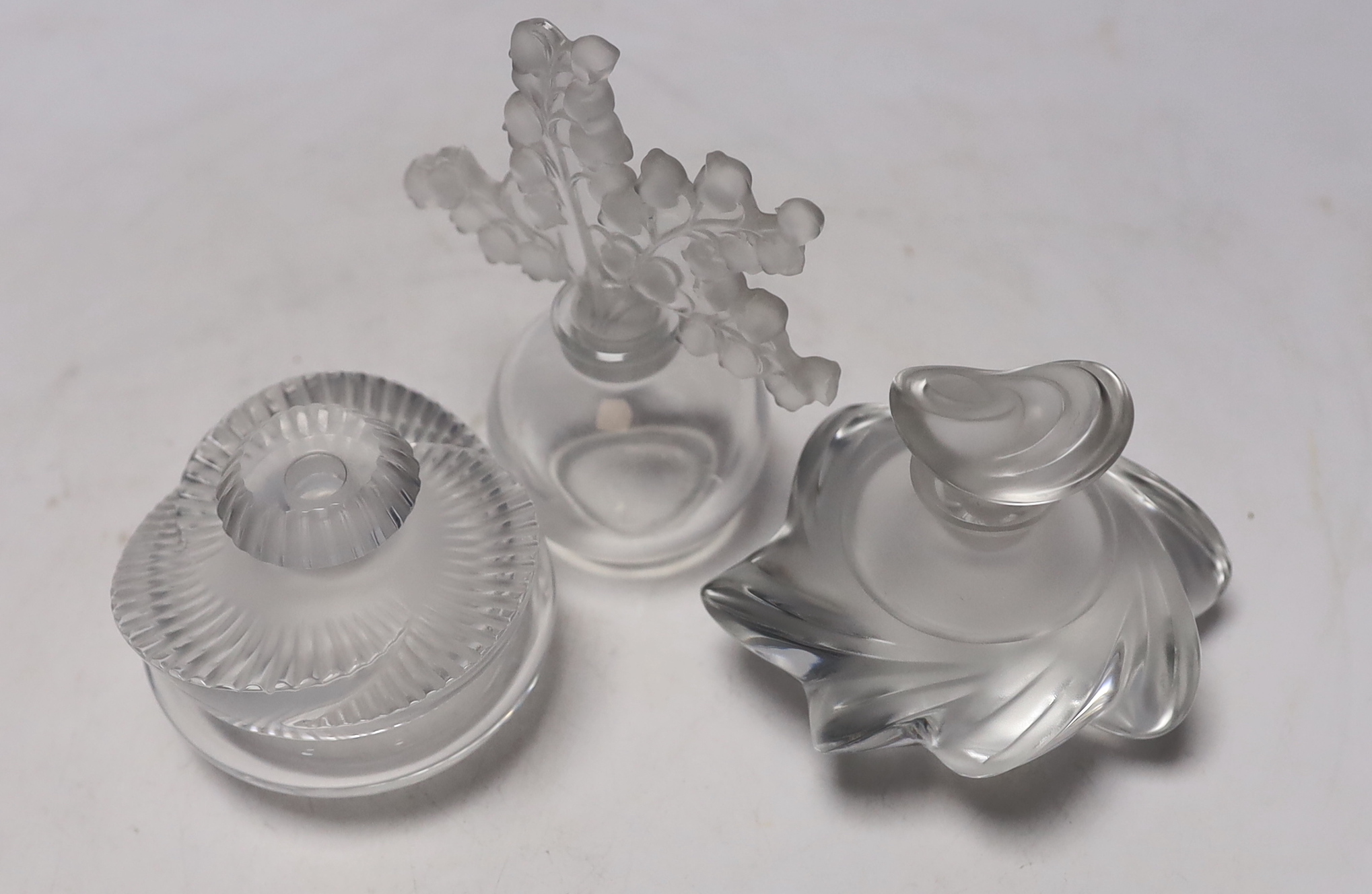 Three Lalique glass scent bottles and stoppers, one with Lily of the Valley stopper, 12cm